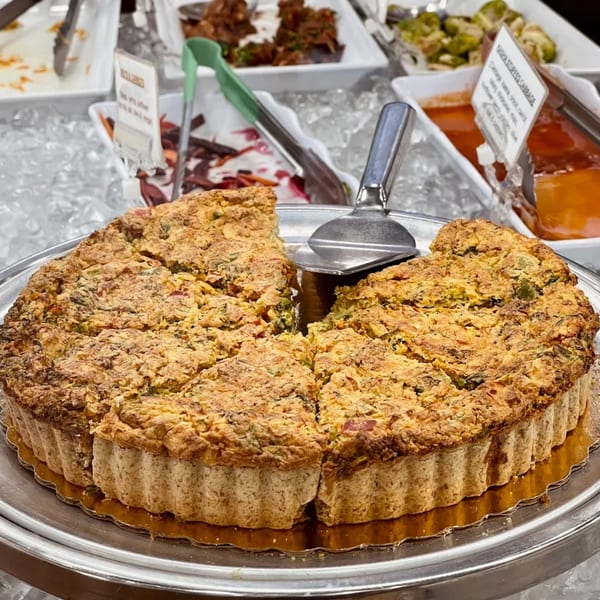 A large, sliced quiche with a golden crust on a silver platter, surrounded by other healthy dishes.