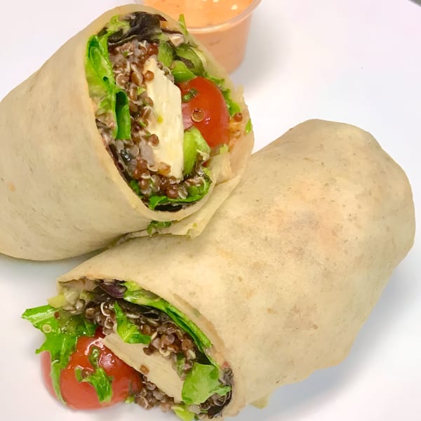 Two healthy Pureganic Cafe wraps filled with quinoa, lettuce, tomatoes, and tofu, with a side of sauce.