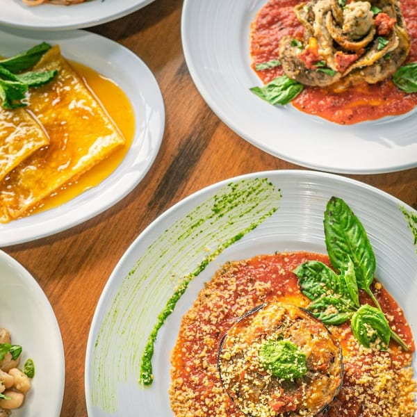 Overhead view of various Italian dishes, including eggplant parmesan, crepes, and pasta, on a wooden table.