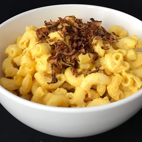 A white bowl filled with creamy vegan mac and cheese, topped with crispy fried onions.