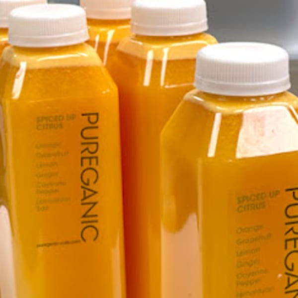 Several Pureganic Cafe "Spiced Up Citrus" juice bottles with orange liquid and white caps.