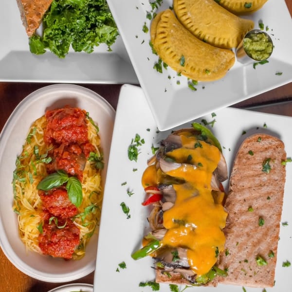 Overhead view of four vegan dishes: spaghetti squash, empanadas, a sandwich, and a salad.