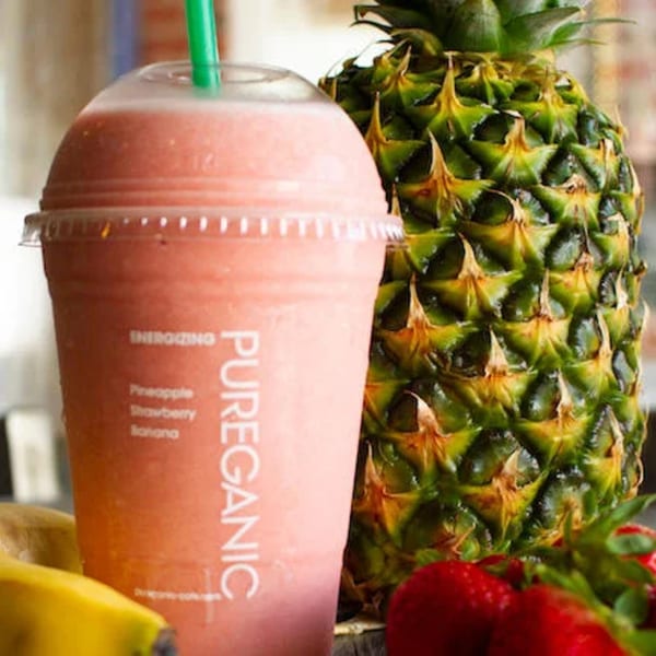 Pureganic Cafe's pineapple, strawberry, and banana smoothie with fresh fruit in the background.